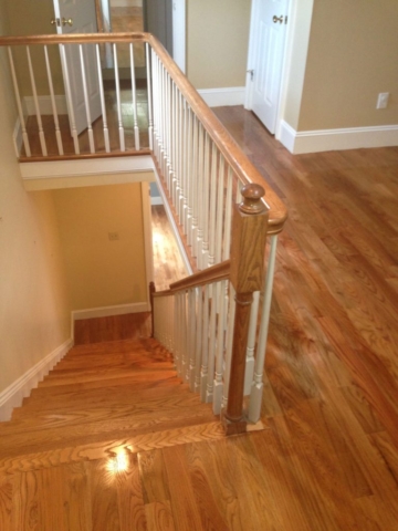 A photo of a staircase and upstairs balcony of newly polyurethaned red oak hardwood flooring.
