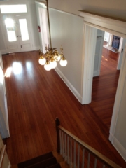 Photo from top of stairs view of an entry foyer of satin finished, red toned, hardwood floors that were previous cover with tar and tile.