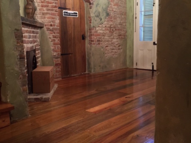 This is a photo of a historic cottage with wide planked pine hardwood floors with shades of red and dark brown.
