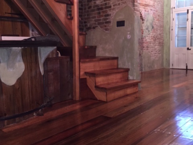 This is a photo of a historic cottage with wide planked pine hardwood floors with shades of red and dark brown. Sanded hardwood staircase is pictured.