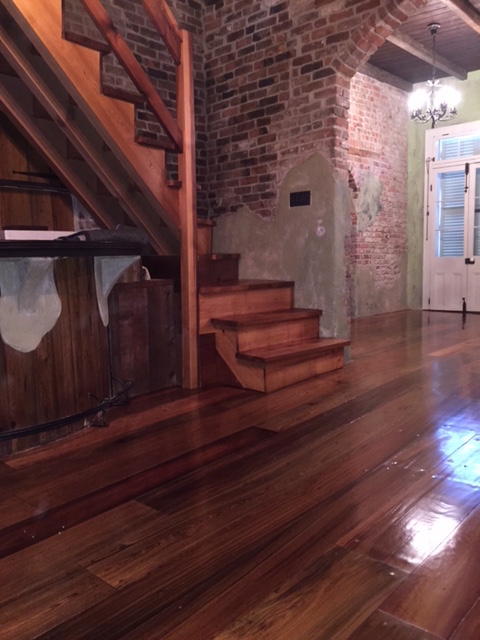 This is a photo of a historic cottage with wide planked pine hardwood floors with shades of red and dark brown. Sanded hardwood staircase is pictured.