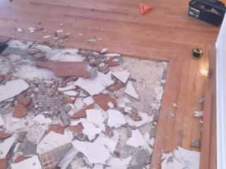 Photo of a square section of broken tile being removed and surrounded by hardwood flooring.