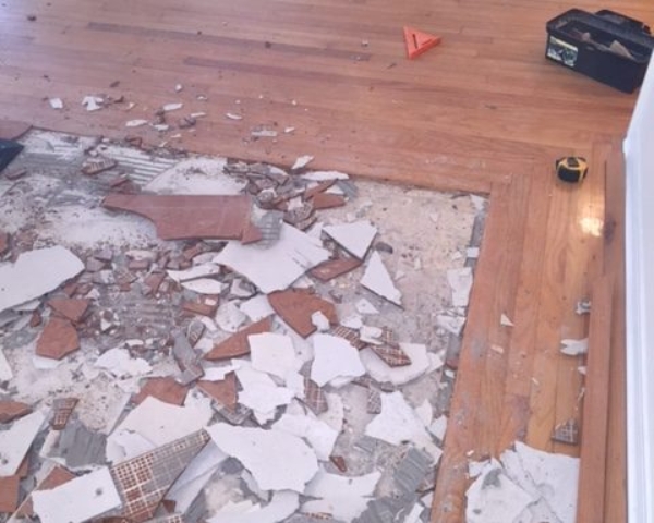Photo of a square section of broken tile being removed and surrounded by hardwood flooring.