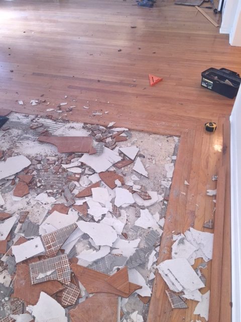 Photo of a square section of broken tile being removed and surrounded by hardwood flooring.