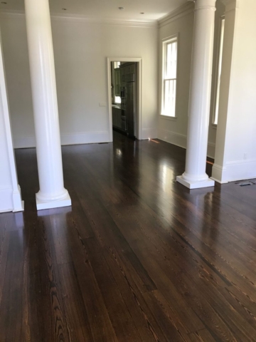 Pictured is a living area of dark stained red pine flooring between two columns.