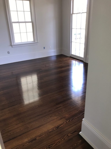 Pictured is a room with dark stained red pine hardwood flooring. It is glossy with the wood grain contrasts visible.