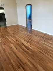 Pictured are red oak floors with a natural finish in a living room with Spanish arched doorways. The contrasting colors in the wood grain are eye catching with shades of red tones, browns, and creamy white.