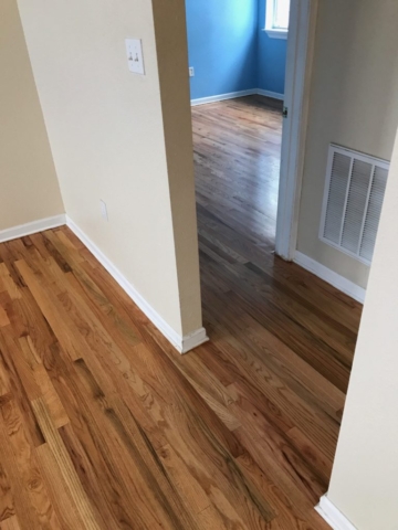 Pictured are red oak floors with a natural finish. The contrasting colors in the wood grain are eye catching with shades of red tones, browns, and creamy white.