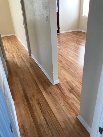 Pictured is a hallway with red oak floors with a natural finish. The contrasting colors in the wood grain are eye catching with shades of red tones, browns, and creamy white.