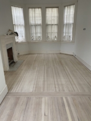 Bleached and white wash finished red oak and red heart of pine in a living room with a bay window and white fireplace. Oak wood is nailed down and visible, called Philidelphia strips.