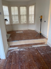 Before photo of red oak and red heart of pine in a living room with a bay window and fireplace