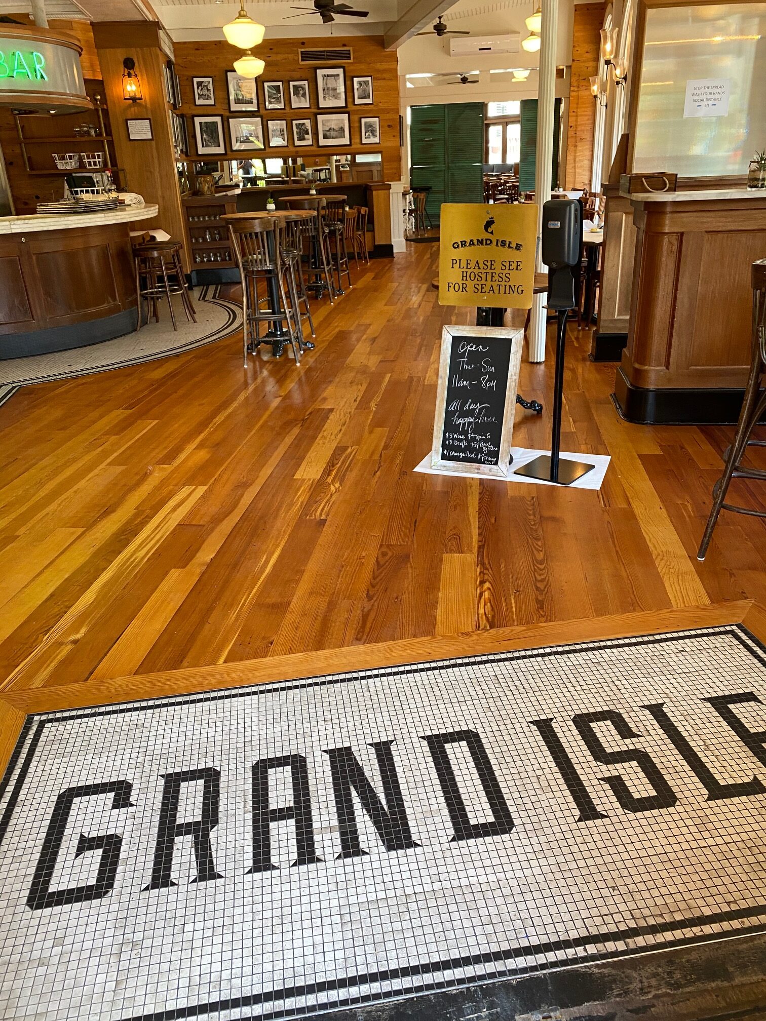 Photo of refinished antique heart of pine floors in a restaurant. Entrance with tiny small tiles reading Grand Isle surrounded by newly finished wooden floors.